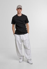 Black cotton t-shirt, loose grey sweatpants, and white sneakers. Gray cap completes the casual look. Plain background highlights outfit.