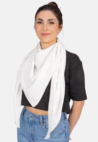 Écharpe carrée blanche et légère drapée autour du cou, avec un motif texturé et froissé. Portée avec un top noir court.