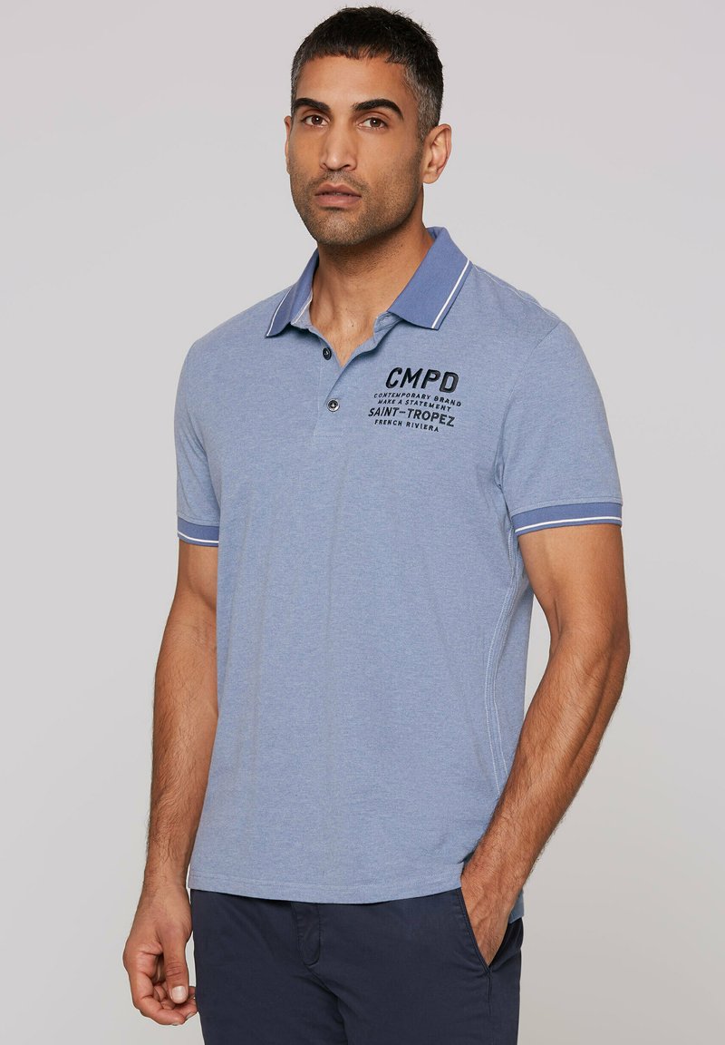 Light blue polo shirt with contrasting collar in darker blue. Features a graphic text print and short sleeves with striped accents.