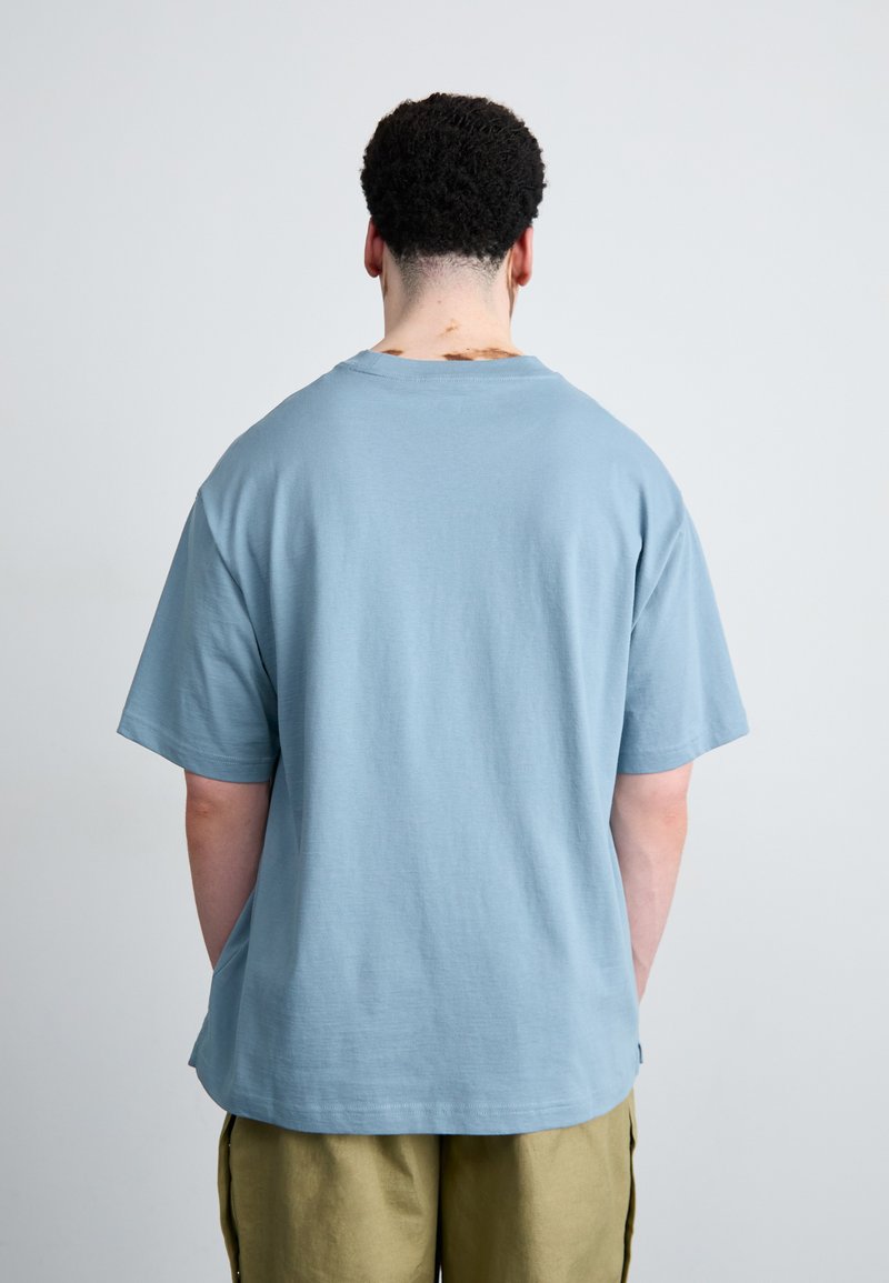 T-shirt en coton bleu clair à manches courtes avec une coupe décontractée. Il présente un col rond et un ourlet légèrement incurvé. Pas de logos ou de motifs visibles.
