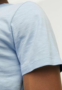 Camisa de manga corta azul claro hecha de una tela suave y texturizada. Detalles de costura en los hombros y un dobladillo limpio y cosido.