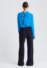 Langwerpige felblauwe blouse met een gestrikt halsstrikje, gecombineerd met hoog-getailleerde, donkerblauwe wijde broek met een gladde textuur.