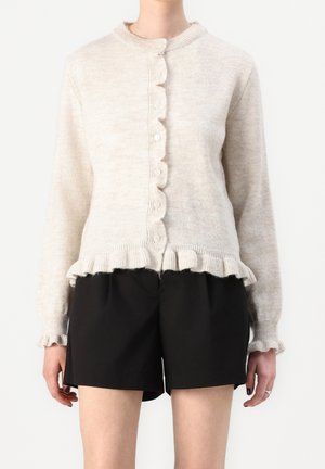 Lichtbeige cardigan gemaakt van zachte stof, met een ronde kraag, knoopsluiting aan de voorkant en een rucheszoom. Gecombineerd met zwarte shorts.