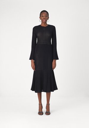 Vestido de punto negro con un cuerpo acanalado, mangas acampanadas y una falda hasta la rodilla. Textura suave con escote ondulado y cintura ajustada.