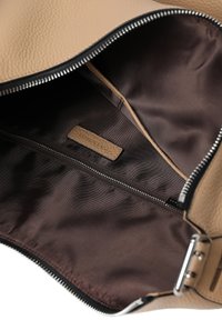 Indvendig beige lædertaske med mørkebrunt foer, der har en lynlåslomme og et lille brunt mærke. Tekstureret ydre med sølvhardware.