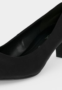 Chaussure femme noire à petit talon, bout fermé avec avant arrondi carré et finition mate lisse sur fond blanc.