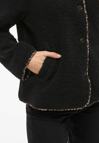 Giacca in pile nera con texture, rifinita con stampa leopardata, chiusure a bottone e tasca laterale sinistra.