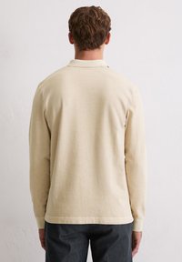 Beige Langarm-Polohemd mit weicher Textur und gerippten Bündchen, ausgestattet mit einem klassischen Kragen und einem geraden Saum.