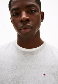 Grå bomulds t-shirt med rund halsudskæring, der har en hvid ribbet krave og en lille logopatch i rød, hvid og blå på brystet.