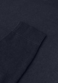 Tummansininen neule, jossa on sileä pinta, ribattu hihansuu ja minimalistinen muotoilu. Kangas näyttää pehmeältä ja kevyeltä.