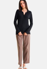 Zwarte geribbelde longsleeve shirt met kraag en knopen aan de voorkant, gecombineerd met beige rechte broek en witte slide sandalen.