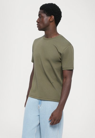 Olivengrøn crewneck t-shirt med korte ærmer, lavet af blød bomuldsblanding, med en afslappet pasform og minimal branding. Lyseblå denimbukser.