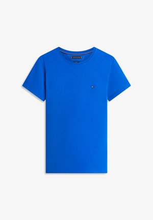 Camiseta azul brillante de cuello redondo y manga corta con pequeño logo de Tommy Hilfiger en el lado izquierdo del pecho sobre fondo blanco.
