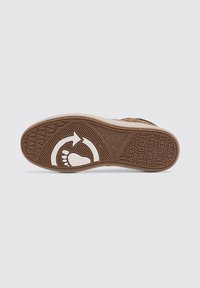 Suela de zapato de goma con una superficie marrón texturizada, que presenta un ícono de pie blanco y flechas. Incluye una marca en relieve y un patrón circular.