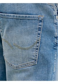 Φωτεινό γαλάζιο τζιν τζινάκι σε κοντινή λήψη, που δείχνει μια πίσω τσέπη με κίτρινη ραφή και διακριτική ξεθωριασμένη υφή.