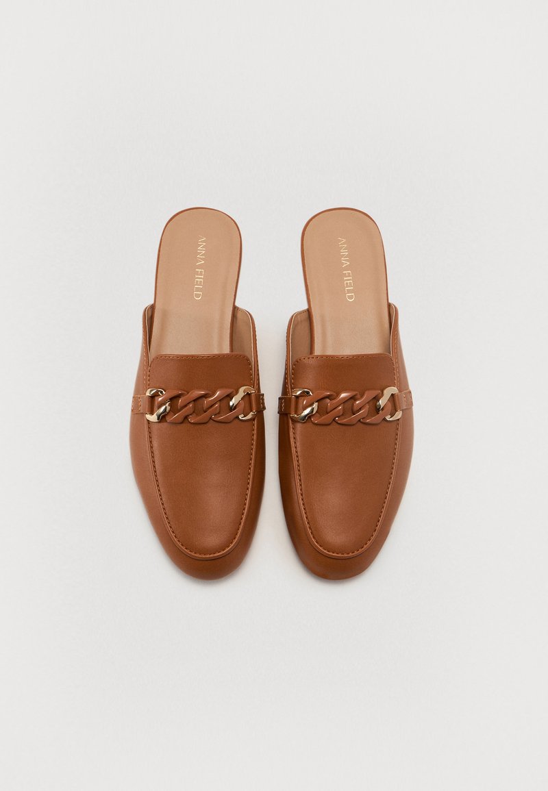 Mules en cuir marron avec une semelle plate, un bout carré et un détail en chaîne sur le dessus. Texture douce avec une finition lisse.
