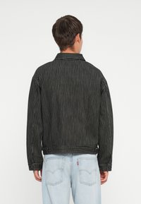 Chaqueta a rayas en blanco y negro con cuello y puños elásticos, con un dobladillo curvado y un corte relajado. La vista trasera muestra un diseño casual.