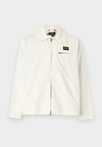 White canvas jacket with a collar, front zipper, two side pockets, and a small black logo patch on the left chest.