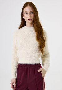 Suéter blanco fuzzy con mangas largas, cuello redondo y una textura suave, combinado con pantalones burdeos que cuentan con franjas laterales.