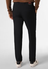 Schwarze, maßgeschneiderte Hose im geraden Schnitt, mit Seitentaschen und glatter Textur. Kombiniert mit weißen Sneakern, die ein minimales Design aufweisen.