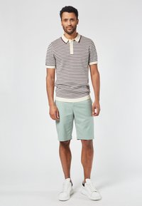 Raidallinen polo-paita vaaleassa kermassa ja burgundinpunaisessa, jossa on kauluskaulus, yhdistetty mintunvihreisiin shortseihin ja valkoisiin lenkkareihin. Rentoa asua.