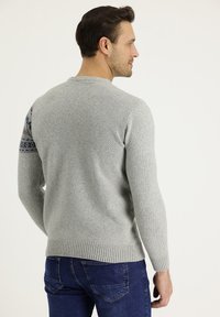Maglione grigio a maglia con orlo e polsini a coste, caratterizzato da un accento a motivo blu e bordeaux sulla spalla sinistra. Indossato con jeans scuri.