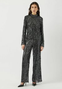 Zwarte pailletten tweedelige outfit met lange mouwen en brede broekspijpen, met verticale franjes en een hoge halslijn.