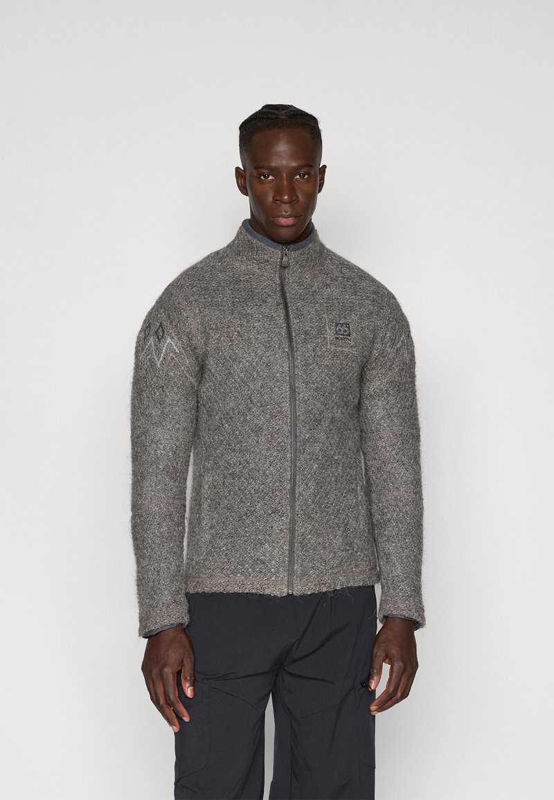 Chaqueta de lana gris con cremallera, con un patrón texturizado y mangas ajustadas, que presenta un alto cuello y un emblema en el lado izquierdo del pecho.