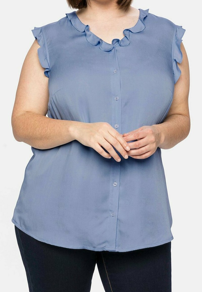 Blusa de color azul claro con cuello acampanado y mangas cortas, que presenta un cierre frontal de botones y una textura de tela suave.