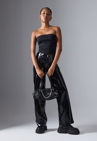 Calças e blusa de couro sintético preto, sapatos de plataforma grossos pretos, segurando uma bolsa preta com detalhes em corrente. Textura suave, design elegante.