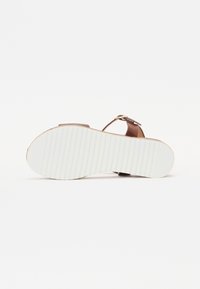 Brown leather sandal with a buckle strap, featuring a textured white rubber sole with horizontal grooves and a round shape.