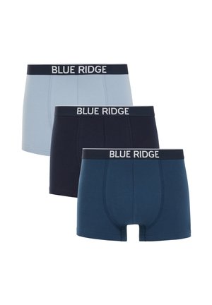 Młody mężczyzna stojący bez koszulki, noszący granatowe bokserki Blue Ridge na jednolitym jasnym tle.