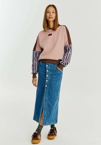 Ružová a hnedá mikina s pruhovanými rukávmi, deninová maxi sukňa s prednými gombíkmi, šedé ponožky a hnedé tenisky. Jednoduchý dizajn a ležérny strih.