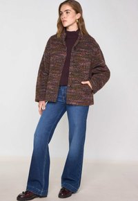 Veste en mélange de laine avec un design texturé et multicolore dans des tons terreux, dotée de grands boutons et de deux poches latérales. Portée avec un jean évasé.