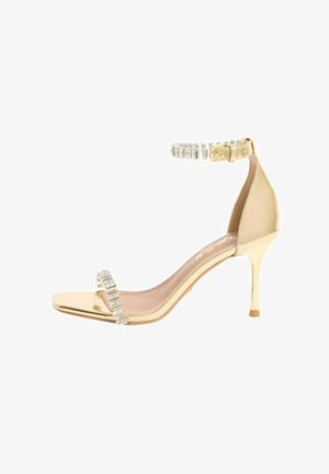 Goldfarbene Stiletto-Sandale mit dünnem Highheel, mit Kristallen besetztem Knöchelriemen und Zehenriemen sowie einem quadratischen offenen Zehendesign.