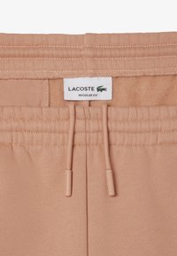 Joggers de algodón color durazno con cintura elástica, que presentan cordones y una etiqueta blanca de Lacoste con un logo verde. Corte regular.