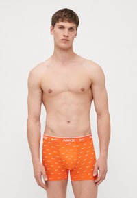 Narancssárga boxer alsónadrág, pamutból készült, fehér Nike logós derékpánttal és ismétlődő fehér swoosh mintázattal. 