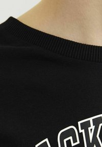 Fekete pamut póló ribbed kerek nyakkivágással; kiemelkedő fehér színű nyomtatott szövegdesign; sima, puha tapintás.