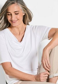 Witte top met cowl-hals en korte mouwen, gemaakt van zacht materiaal met een drapering ontwerp. Te combineren met lichtbeige broeken, die een relaxte pasvorm laten zien.