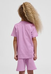Lyserød bomulds t-shirt med korte ærmer, der er sat sammen med matchende shorts. Stoffet er blødt, og begge dele har en afslappet pasform.