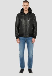 Veste en cuir noire avec capuche, fermeture éclair et poches avant. Portée avec un jean bleu clair et des baskets noires. Design classique décontracté.