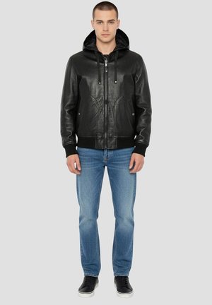 Zwarte leren jas met capuchon, ritssluiting en voorkantzakken. Draagt over lichtblauwe spijkerbroek en zwarte sneakers. Klassiek casual ontwerp.