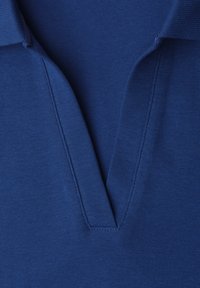 Dettaglio del colletto e della scollatura di una polo blu realizzata in tessuto a maglia strutturata, mostrata piatta senza bottoni o decorazioni.