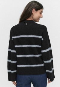 Svart och grå randig tröja med en mjuk, fluffig textur, vida ärmar och en cirkulär detalj vid nackens baksida.