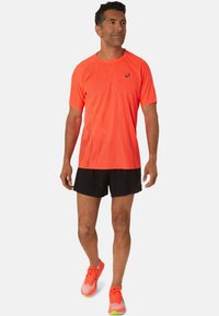 Bright orange, short-sleeved athletic shirt with textured pattern; paired with black shorts and orange running shoes with green accents.