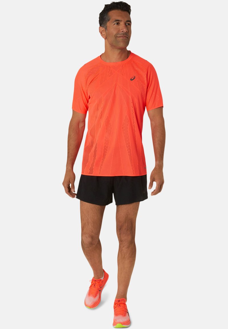 Bright orange, short-sleeved athletic shirt with textured pattern; paired with black shorts and orange running shoes with green accents.
