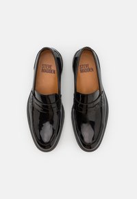 Mocassins en cuir verni noir avec une finition lisse, dotés d'un bout arrondi, de coutures décoratives et d'une semelle intérieure marquée.