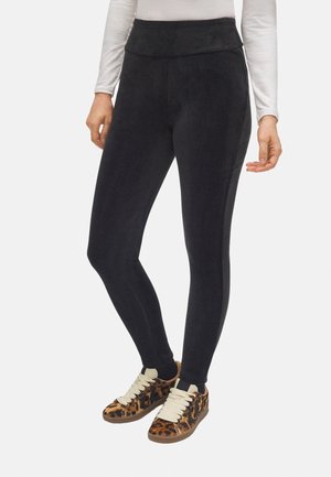 Leggings negras con relieve y cintura alta. El material parece suave y texturizado. Combinadas con zapatillas de leopardo que tienen cordones crema.