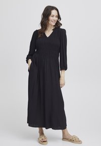 Schwarzes Maxikleid mit einem gerafften Oberteil, langen Puffärmeln und einem V-Ausschnitt. Glatte Textur, fließender Stoff und seitliche Taschen.