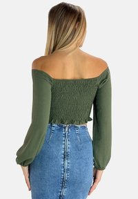 Top verde oliva con scollo a barca, dettagli arricciati e maniche lunghe, abbinato a una gonna di jeans a vita alta con una silhouette aderente.